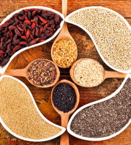 Goji berries, amaranth seeds, chia seeds, kinoa seeds in the ceramic bowls and linen, sesame, nigella in wooden spoons. Nutritional supplement on wooden background. Text space.